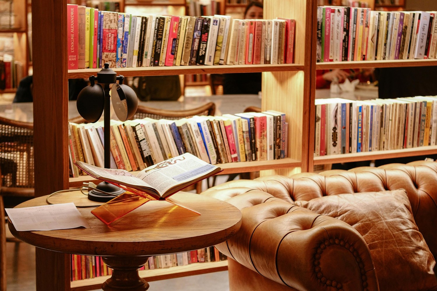 An open book, reading lamp, and chair beside full bookshelves