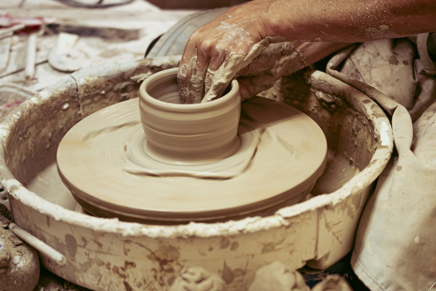 A potter shaping the rim of a clay vessel on a wheel